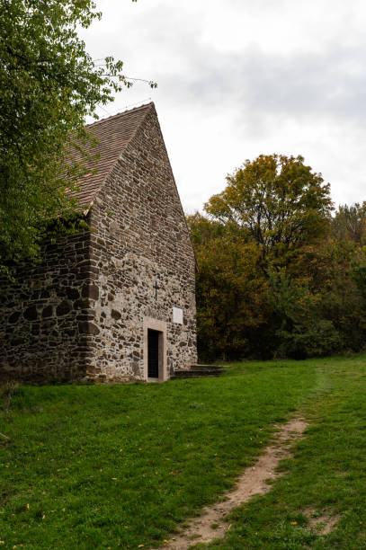 A historic stone chapel surrounded by autumn trees stands in a peaceful rural setting in Hungary. The rustic architecture and weathered stone walls evoke a sense of historical charm and tranquility.