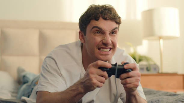 istock Playful Caucasian European young man lying on bed playing console holding joystick video games fun weekend home enjoy guy hobby leisure hands technology virtual cyberspace cheerful excitement smiling 2181380791