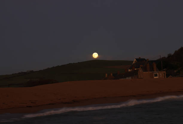 Full Moon rising above hill towards breaking waves
