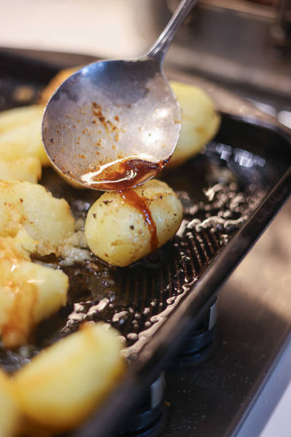 Basting part cooked roast potatoes in meat juices in a hot roasting pan