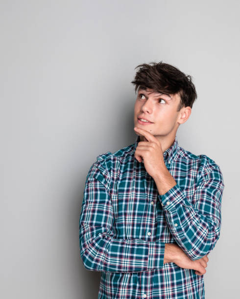 istock pensive young guy wearing plaid shirt and thinking while touching chin 2181386993