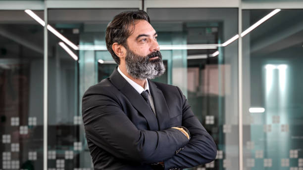 istock A middle-aged, dark-haired, bearded businessman stands in an empty office environment with a blurred background, arms crossed, smiling as he looks at the camera 2181389722