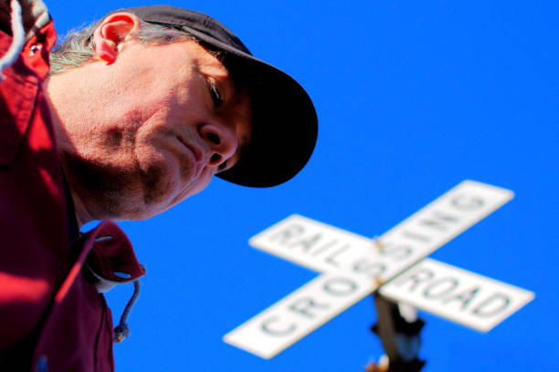 Low angle view of an adult Caucasian middle aged  man passing by a railroad sign.