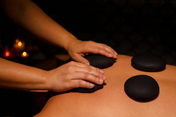 istock Woman's hands giving man stone therapy using black hot stones in Thai massage parlor by candlelight 2181392758