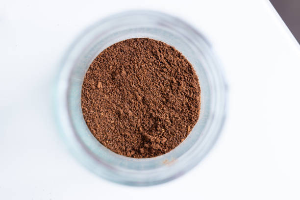 Glass jar filled with ground coffee sitting on a white background, ready to be brewed