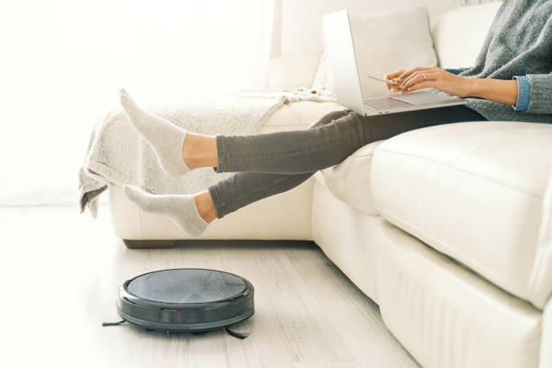 istock Female freelancer raising legs above working robotic vacuum clea 2181397720