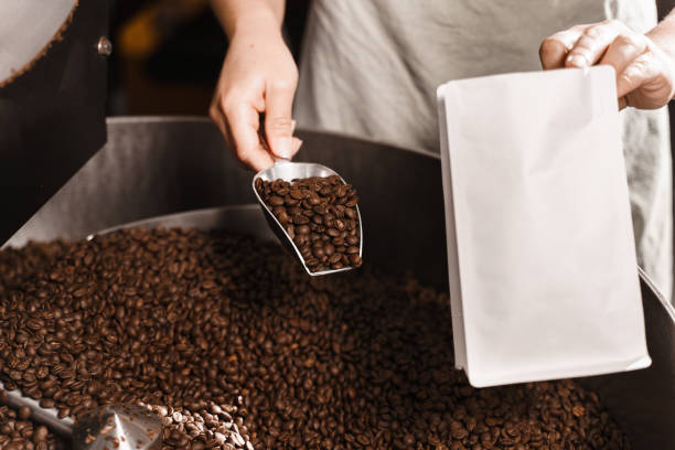 istock Filling coffee grains in a craft bag. Packing fried coffee beans. Worker pouring roasted coffee beans in packaging bag. 2181407574