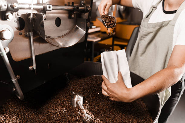istock Packing roasted coffee beans into a craft bag. Pouring fried coffee grains in packaging bag in the facility. 2181407607