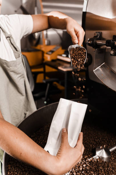 istock Pouring fried coffee grains in packaging bag in the facility. Packing roasted coffee beans into a craft bag. 2181407610