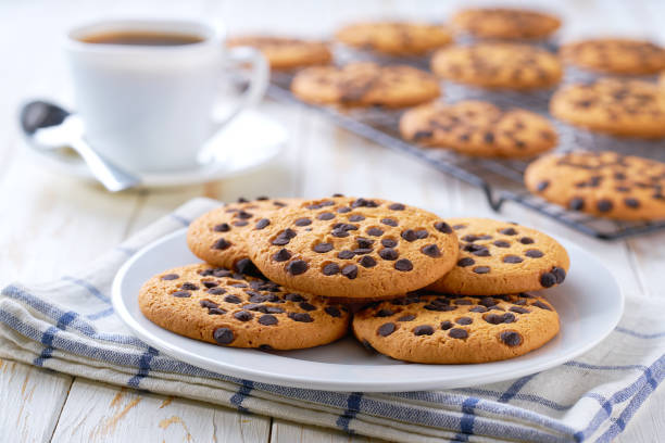 Tasty cookies with chocolate chips and coffee on a light kitchen table, selective focus.