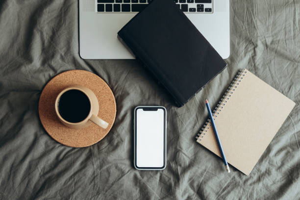 istock Blank screen phone, laptop and coffee cup on the grey bed sheet. 2181431878