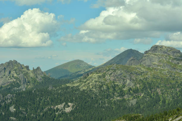 istock A high mountain range overgrown with a dense coniferous forest with unusually shaped pointed peaks under a cloudy summer sky. 2181436572