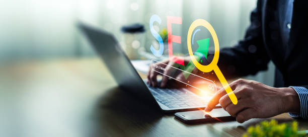 istock Digital Marketing Concept with SEO Optimization, Search Bar, and Analytics on Laptop Screen, Man's Hand Interacting with Smartphone for Online Business Strategy 2181436584