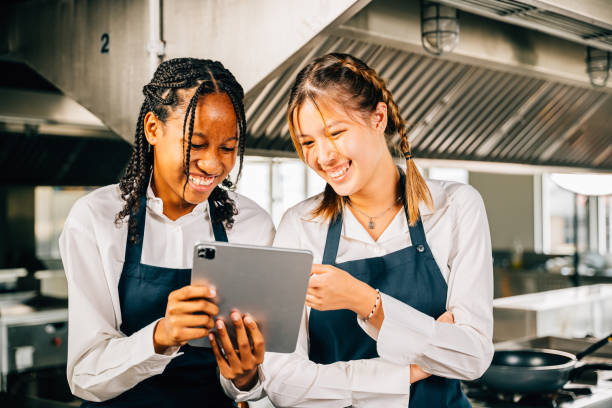 istock Two famous chefs in a professional stainless steel kitchen discuss their video blog using a tablet. Professionals smiling standing reading searching utilizing modern technology. 2181442044