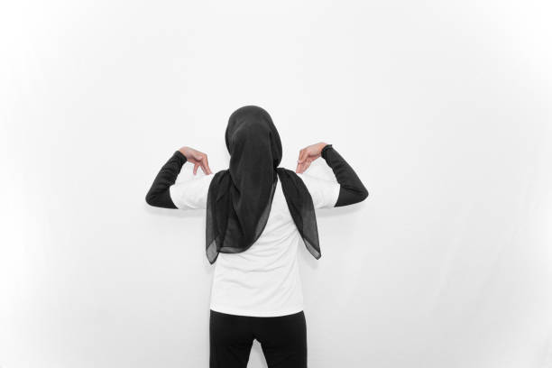 A woman in a white hijab does gymnastics, facing backwards with both hands bent to her shoulders.