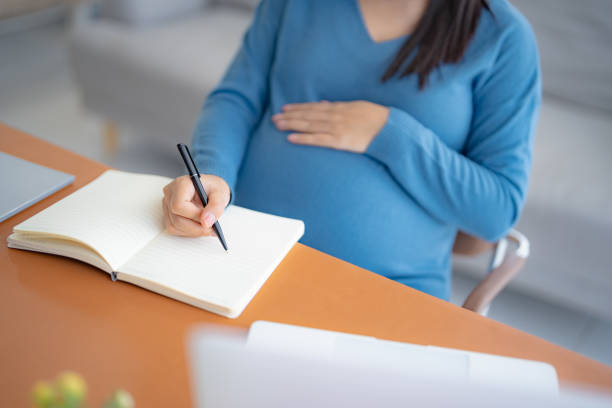 istock Pregnant asian woman writing notes and using a laptop while working at home pregnantÂ businesswoman workingÂ on remote project in home office pregnancy concept 2181453984