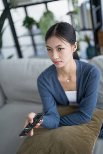 istock Asian woman Watching smart TV and using remote controller Hand holding television audio remote control at home with the remote control television 2181453989