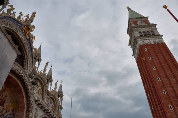 Upward view of the iconic Campanile of St. Mark's Square, Venice, Italy. This towering Gothic bell tower dominates the skyline and stands in striking contrast to the intricate facade of St. Mark's Basilica.