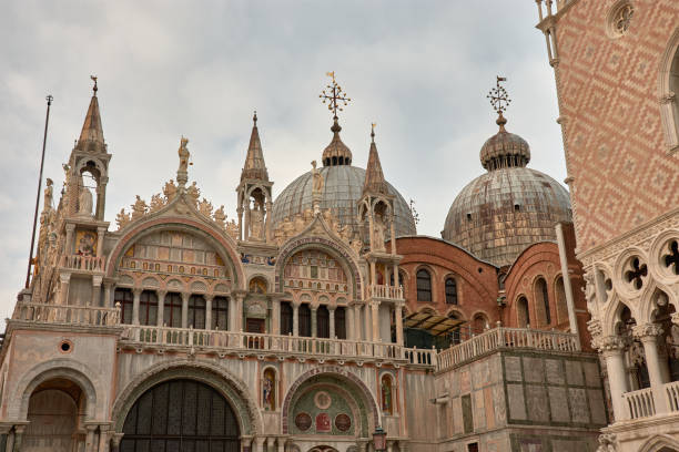 A captivating view of St. Mark's Square in Venice, Italy, showcasing the grandeur of the historic piazza. The square is flanked by the majestic St. Mark's Basilica, the towering Campanile, and the elegant arcades of the Procuratie buildings. The lively atmosphere is filled with visitors, outdoor cafes, and pigeons, epitomizing the heart of Venice's cultural and social life.