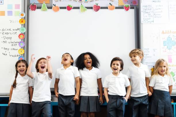 Group of diverse children students smiling in a classroom. Kids standing, laughing, and having fun in front of white board classroom. Classroom setting with students enjoying. Students enjoying class