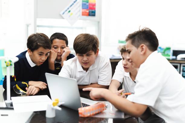 Group of student boys focus on laptop, collaborate in classroom.