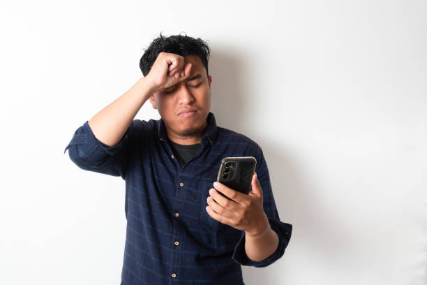 istock Asian man holding his mobile phone with sad expression 2181458309