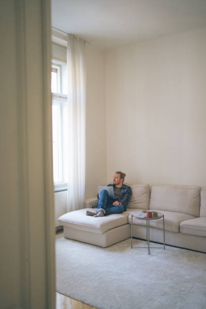 istock Young man works on laptop on living room couch 2181461281