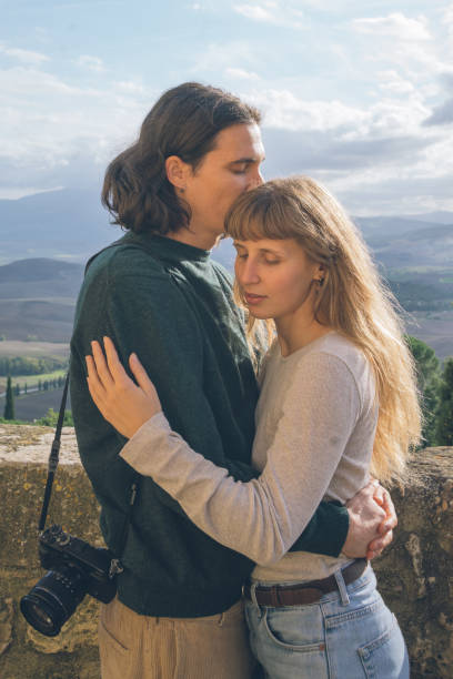 Young hipster couple embrace on hilltop above valley, Tuscany