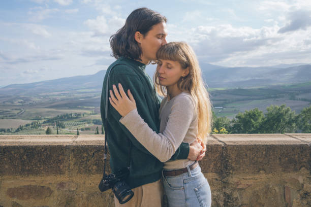 Young hipster couple embrace on hilltop above valley, Tuscany