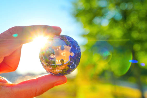 Hand Holding Puzzle Globe with Sunlight and Green Background
