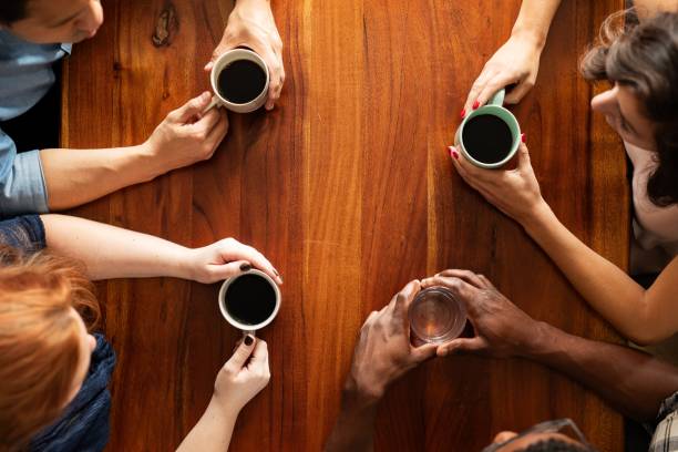 Diverse group of people having coffee. Top view of hands holding coffee cups. Coffee meeting with diverse hands. Coffee and conversation among diverse group of people. Diverse people drinking coffee