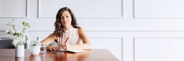 A woman sits at a desk, writing in a notebook.