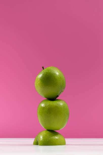 istock Lush green apples stack balances on vibrant pink background 2181481833