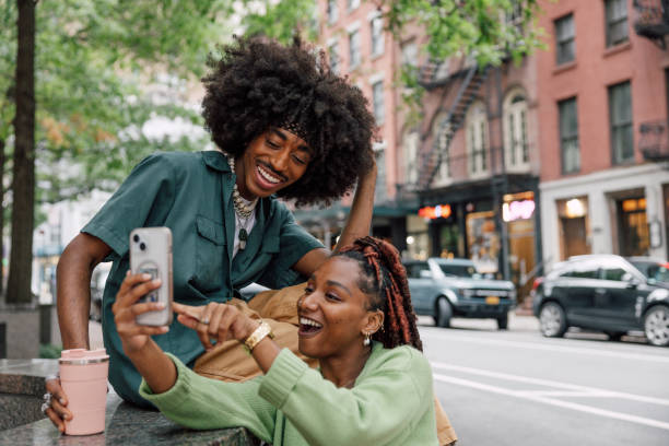 istock Two friends in using mobile phone outdoors sitting on bench 2181482327