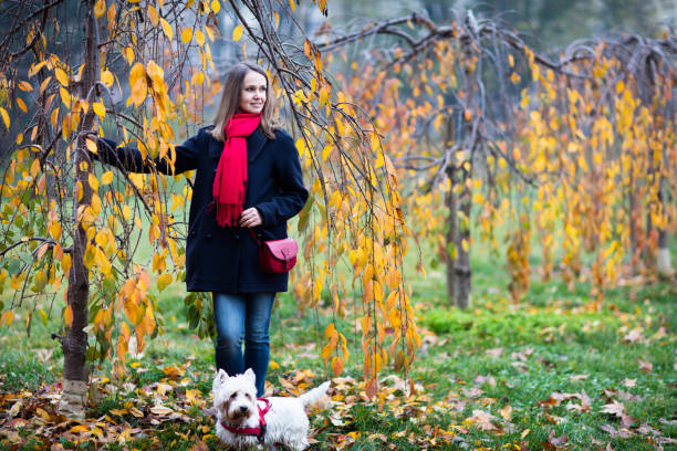 There are many beautiful and huge parks in Turin that turn red, orange and yellow in autumn. Here is Valentino Park, under some Japanese cherry trees a beautiful woman stands with her cute little dog .