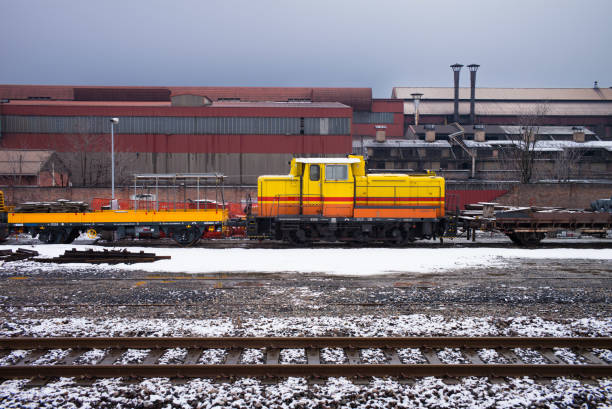 It is a hazy, gloomy day in Aosta, near the steel mill. It has snowed a little, a colorful train stands out on the gray day.