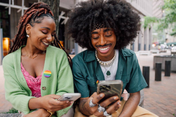 istock Two friends in using mobile phone outdoors sitting on bench 2181482644