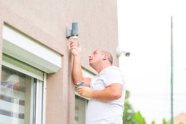 Electrician changing light bulb on house wall holding electric screw driver