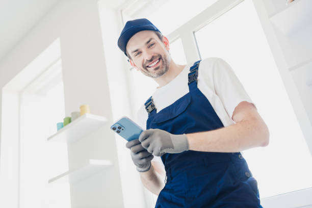 istock Smiling handyman in blue overalls using smartphone during home renovation in bright modern apartment 2181487994