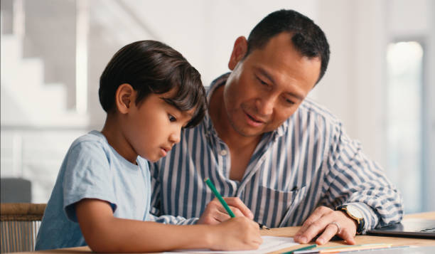 istock Japanese dad, boy and writing with homework in home for education, learning and support with care. Parent, helping and people for child development or growth with project, art and creativity 2181488717