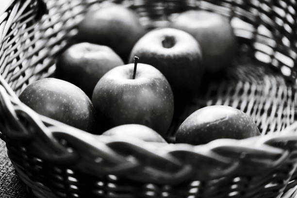 Fresh apples arranged in a traditional wicker basket, monochrome.