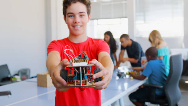 istock Portrait Of Smiling Male Student Holding Robot Vehicle Built In School Computer Coding Class 2181490360