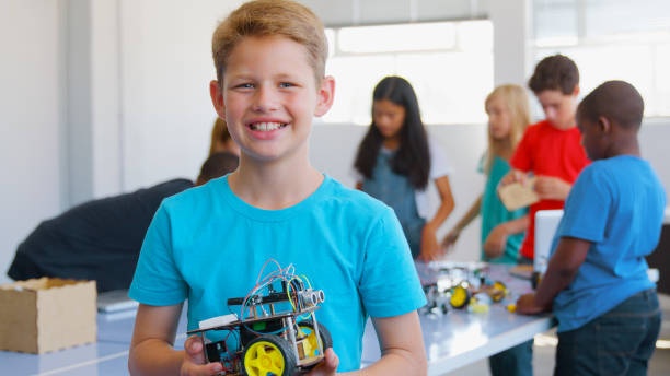 istock Portrait Of Smiling Male Student Holding Robot Vehicle Built In School Computer Coding Class 2181490367