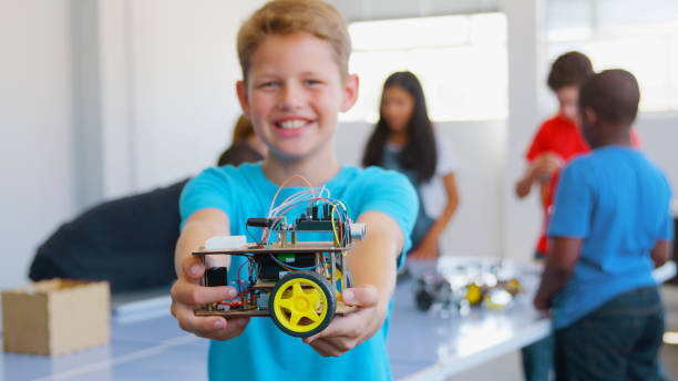 istock Portrait Of Smiling Male Student Holding Robot Vehicle Built In School Computer Coding Class 2181490422