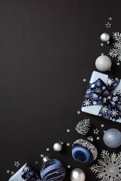 istock Elegant Christmas or winter holidays decorations featuring silver and blue gift boxes, silver baubles, pine cones, and white stars on a dark background. Flat lay, top view, vertical 2181495484