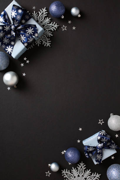 istock Stylish Christmas decorations featuring silver and blue gift boxes, silver baubles, pine cones, and white stars on a dark background. Flat lay, top view, vertical 2181495693