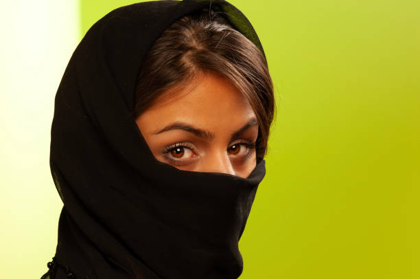 Close up of a young Iranian woman wearing a hijab looking at the camera on green background. Front view.