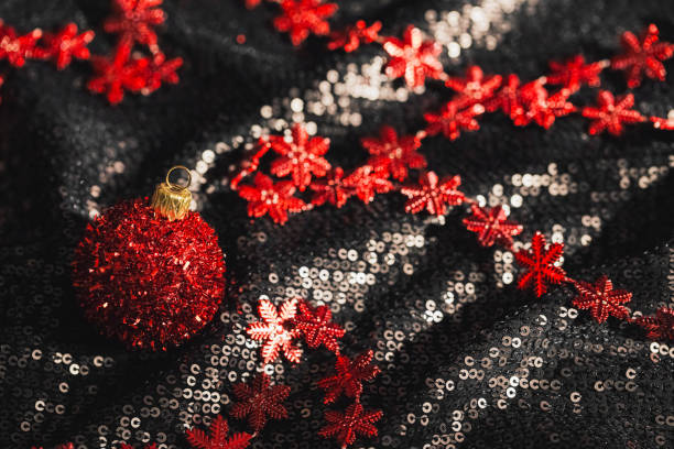 Red christmas bauble on shimmering black background with sequins. Minimal style xmas composition. Celebration and party concept