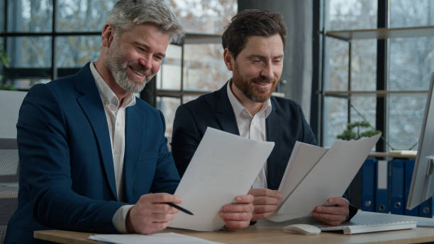istock Two Caucasian men businessmen in office working together on financial statistics analyzing charts project discussing data in report doing paperwork using computer looking documents client consultation 2181511377