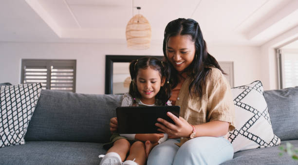 istock Happy, woman and child with tablet on sofa for knowledge, development or education game together. Living room, smile and girl with tech by mother for interactive, elearning or quiz on website at home 2181522639
